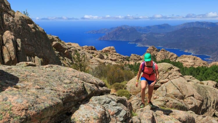 Randonneuse sur un sentier rocheux avec vue sur le littoral corse.