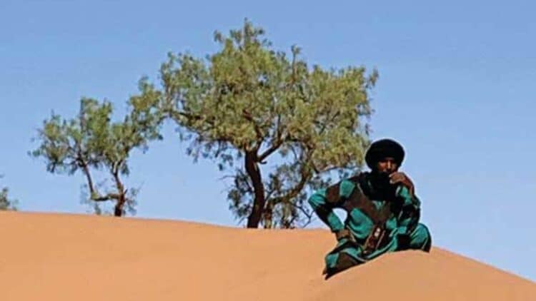 Homme assis sur une dune de sable dans le désert marocain.