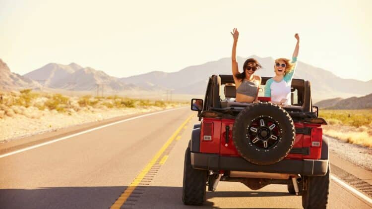 Couple de femmes voyageant en 4x4 sur une route au cœur de paysages montagneux.