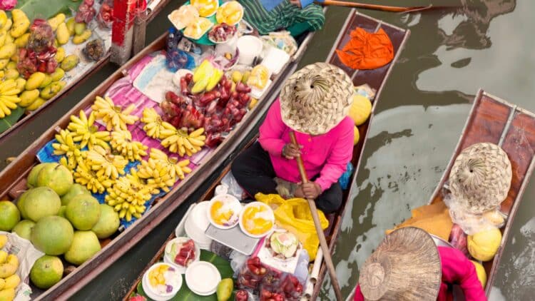 Marché flottant en Thaïlande avec des vendeurs proposant des fruits frais depuis leurs embarcations.
