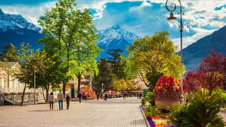 Promenade fleurie dans une ville du Tyrol avec les Alpes en arrière-plan.